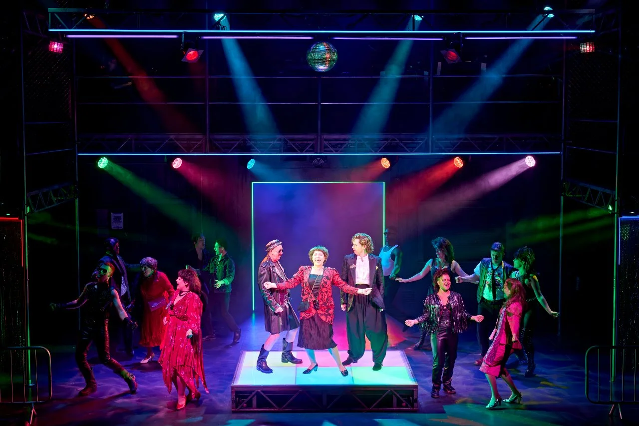 Cast of Pride the Musical dancing under a disco ball at the National Theatre