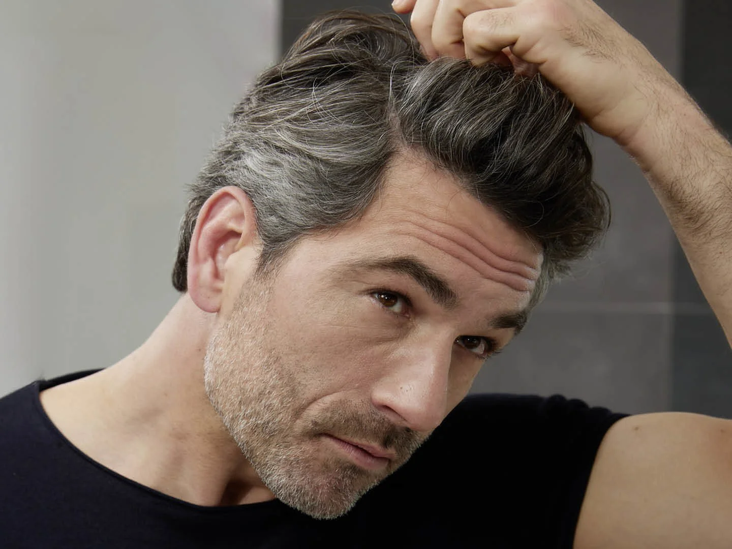 Man examining grey hair science mix of grey and dark strands at his hairline