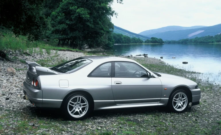 a stunning silver Nissan Skyline R33 GTR besides a lake