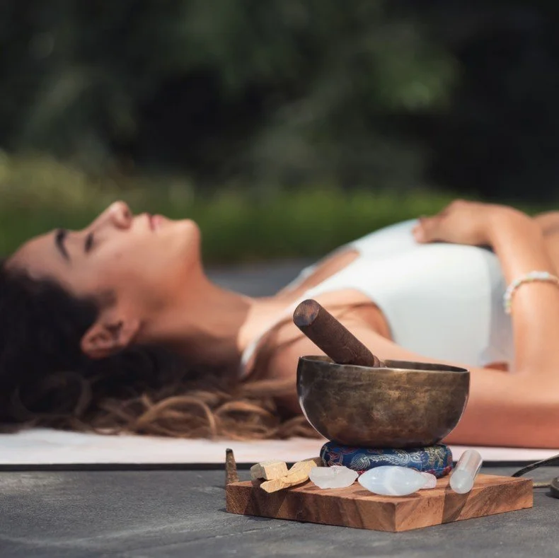 Woman lying down relaxed during an outdoor breathwork session with a singing bowl nearby