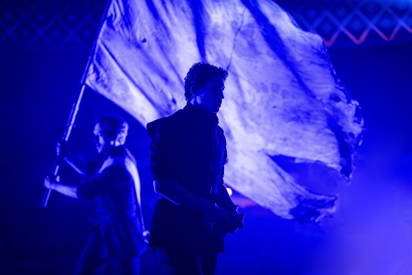 Martin Guerre cast members under blue light with a war banner at the Old Vic